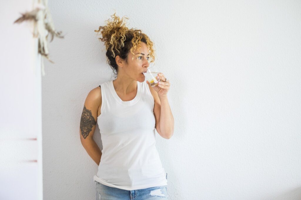 Attractive curly blonde middle age cute woman drinking water and lemon at home