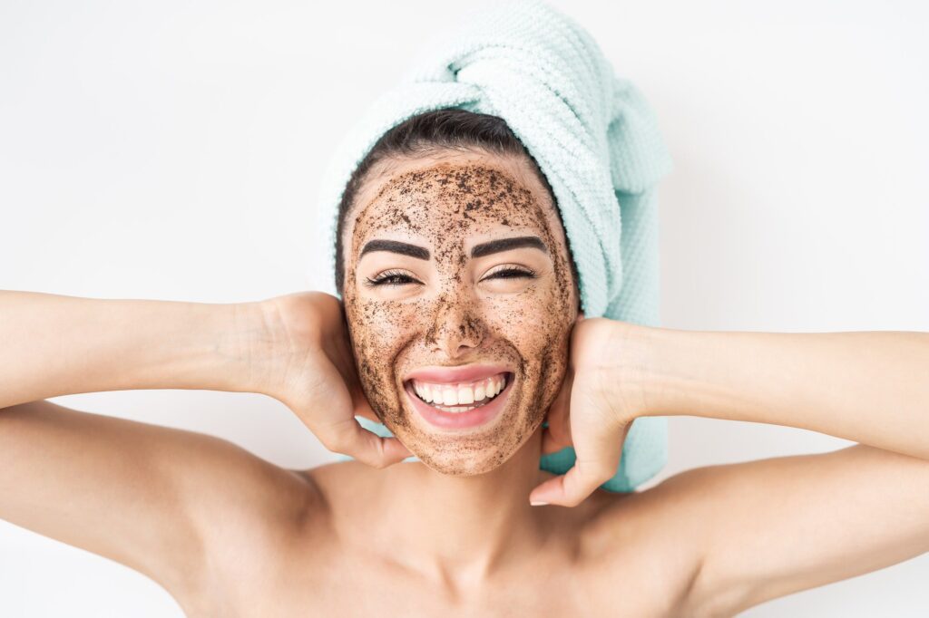 Young smiling woman applying coffee scrub mask on face