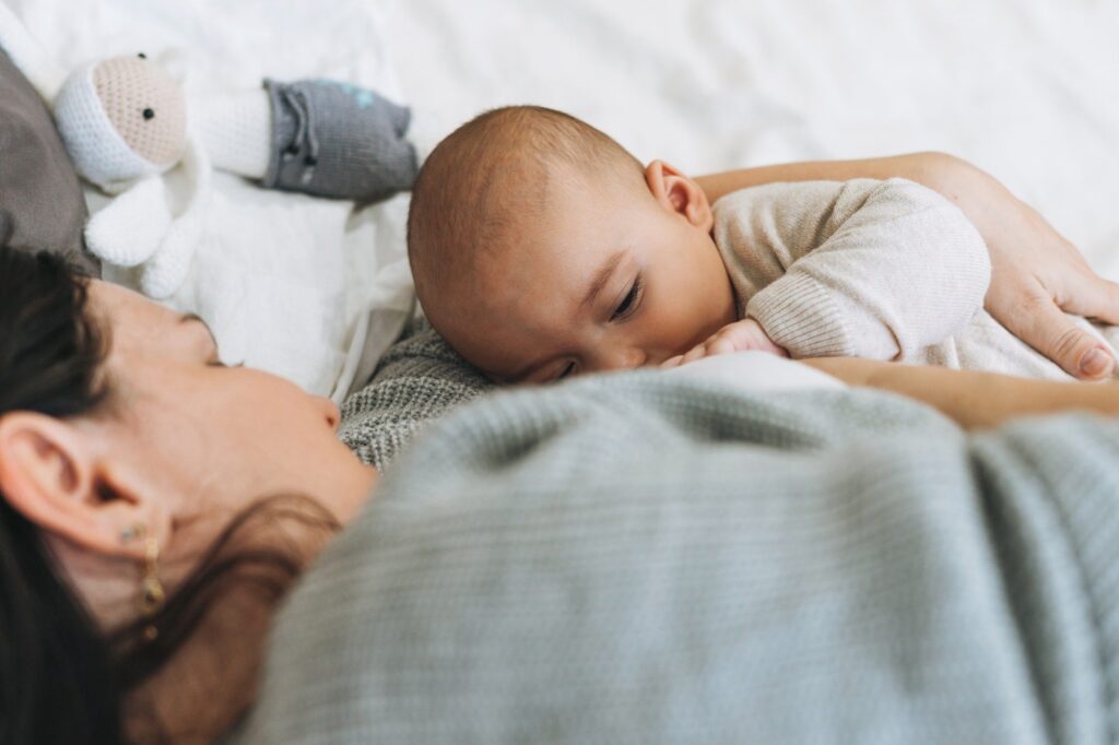 Young mom with cute baby boy, mother breast-feeds baby on bed