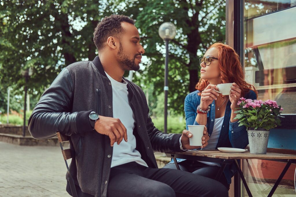 A couple dating drinking coffee, sitting near the coffee shop. Outdoors on a date.