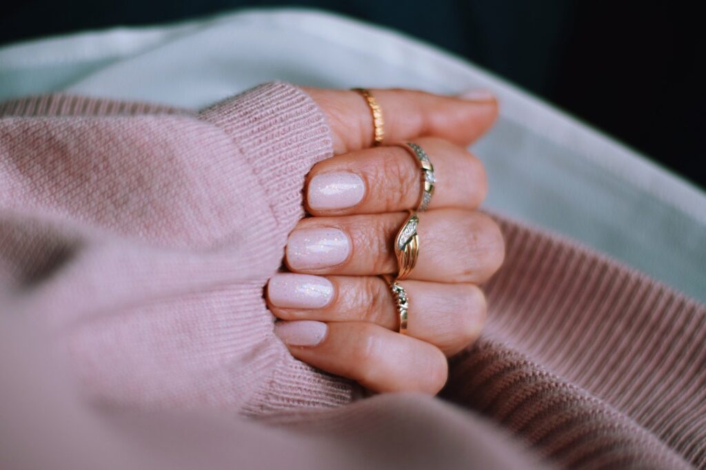 Blush pink nails with sparkles, gold rings and a pink sweater