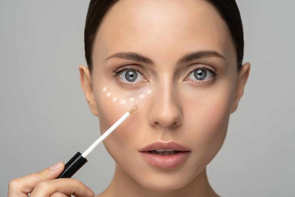 Woman with natural makeup applying corrector on flawless fresh skin, put concealer under eye area.